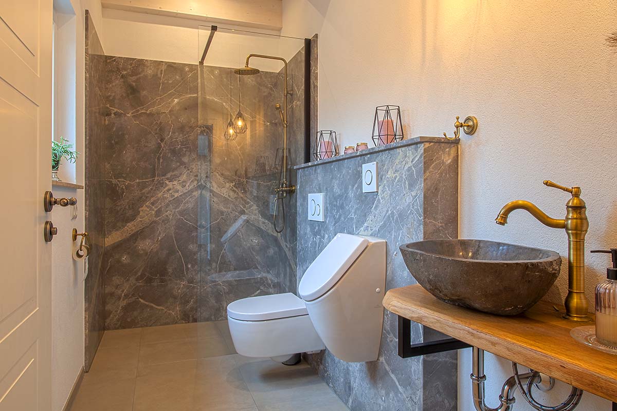 Naturstein Bad mit eleganter Dusche, Steinwaschbecken und goldener Armatur